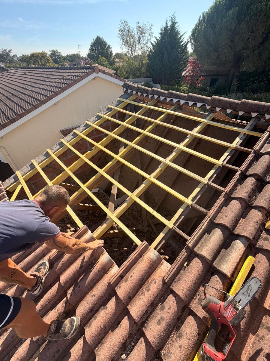 Couvreur fixant des liteaux sur une toiture partiellement déposée à Tautavel, chevrons contrôlés